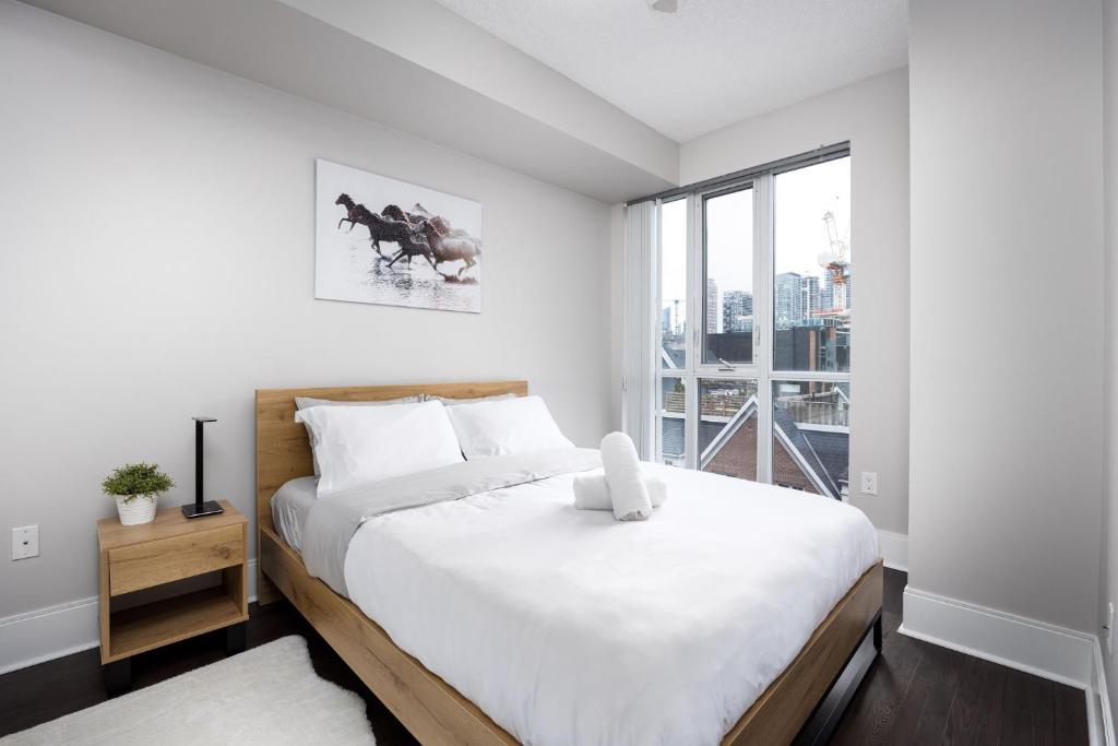 a white bedroom with a large bed and a window at DWTN Condo Near CN Tower! w/ Free Parking in Toronto