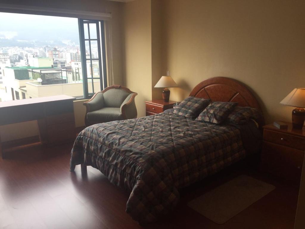 um quarto com uma cama, uma cadeira e uma janela em Departamento Amoblado em Quito