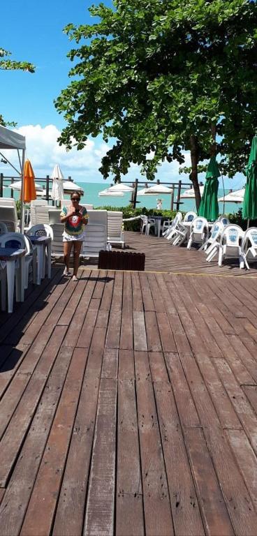 Resort All Inclusive Arcobaleno في بورتو سيغورو: امرأة تقف على سطح خشبي مع طاولات وكراسي