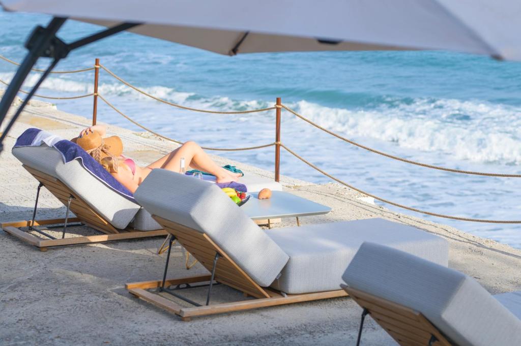 a woman laying in lounge chairs on the beach at Iconic PRIVE beachfront villa Mola Kaliva in Mola Kalyva