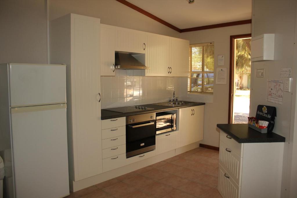 a kitchen with white cabinets and a sink and a refrigerator at Ningaloo Coral Bay – Bayview in Coral Bay