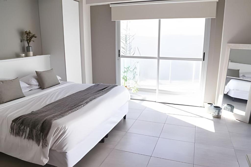 a white bedroom with a large bed and a large window at Charlie Suites en el casco histórico de Salta in Salta
