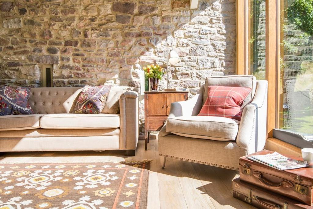 a living room with two chairs and a stone wall at Williamston Barn in Slaggyford