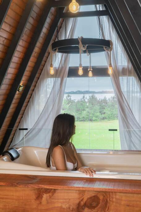 a woman sitting in a bath tub looking out a window at Refúgio Romântico com Jacuzzi na Natureza a 10 min da Praia in Torres