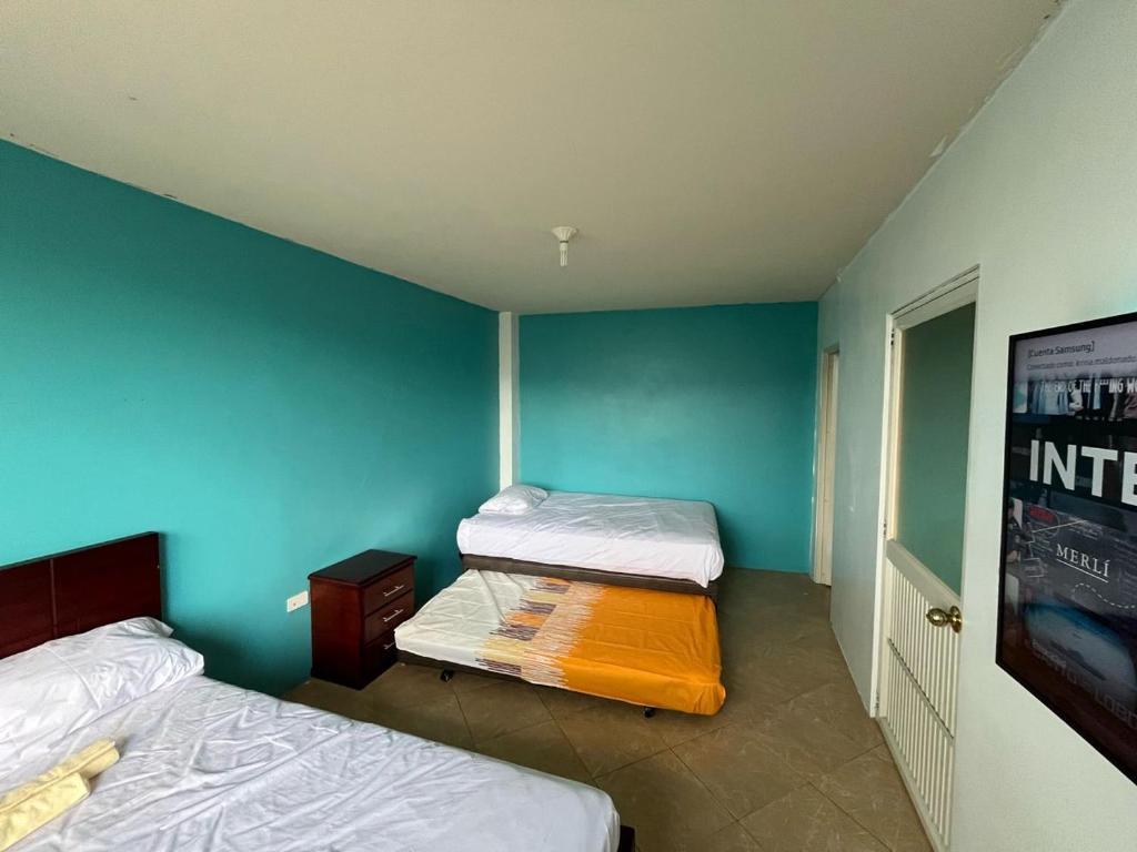 two beds in a room with blue walls at La Orquidea Airbnb in Piñas