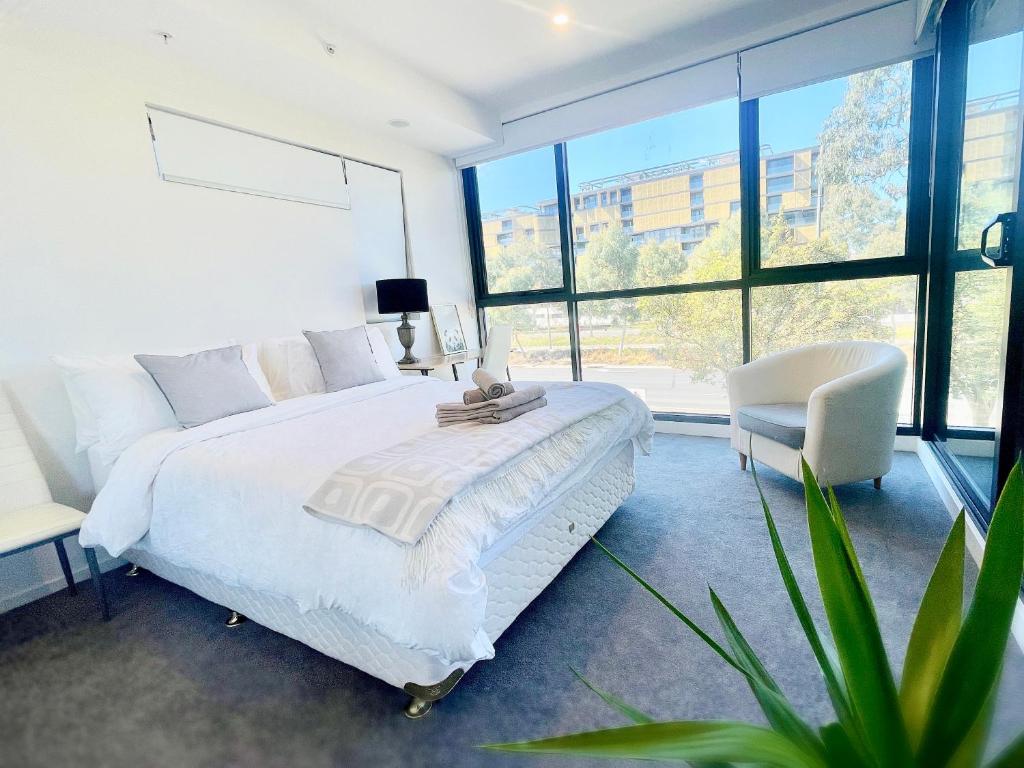 um quarto com uma cama branca, uma cadeira e janelas em Brand New Stylish 1BR Apartment, Specious Space, Free Parking, Self Check-in em Canberra