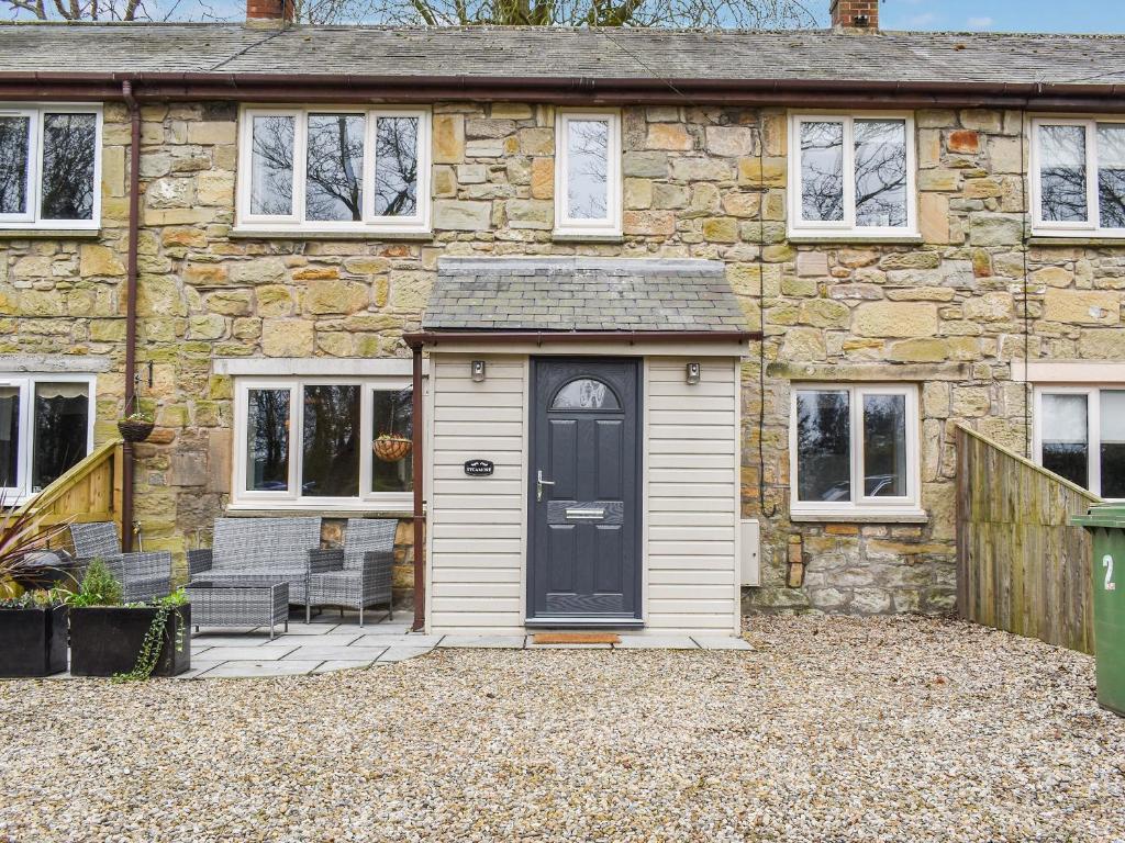 a stone house with a black door and two chairs at Sycamore Cottage in Broomhill
