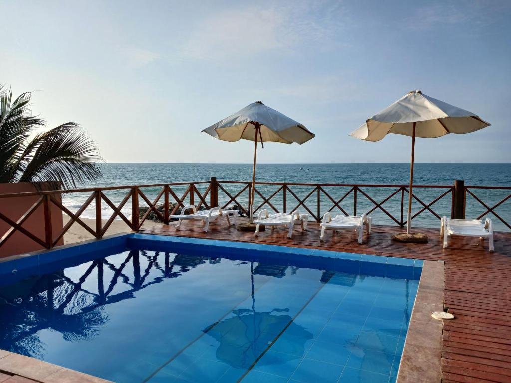 a swimming pool with umbrellas and chairs and the ocean at Casa de Playa Akas in Canoas de Punta Sal