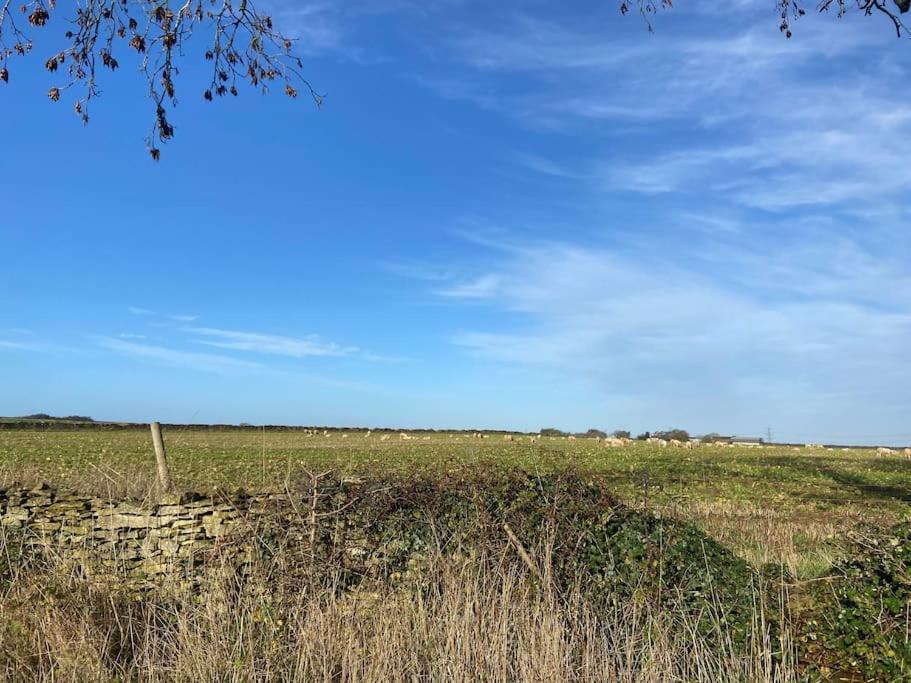 a field with a stone wall and a blue sky at Beautiful Scenic Holiday Chalet in Lincolnshire