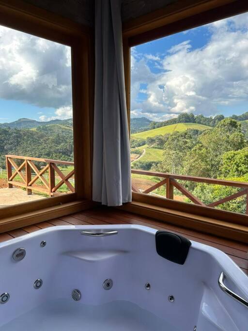 Una bañera en una habitación con una ventana grande. en Chalé Recanto das Estrelas, en Monte Verde