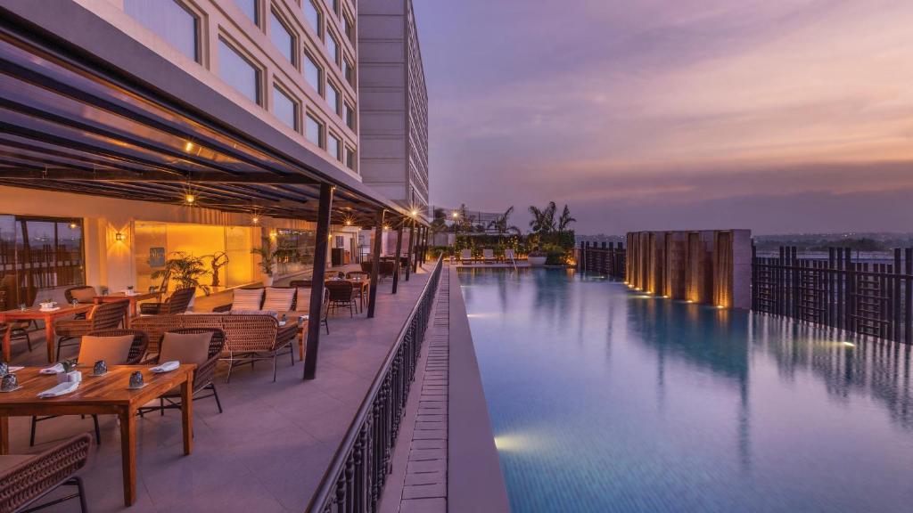 una piscina de hotel con mesas y sillas junto a un edificio en Holiday Inn New Delhi Mayur Vihar Noida, an IHG Hotel en Nueva Delhi