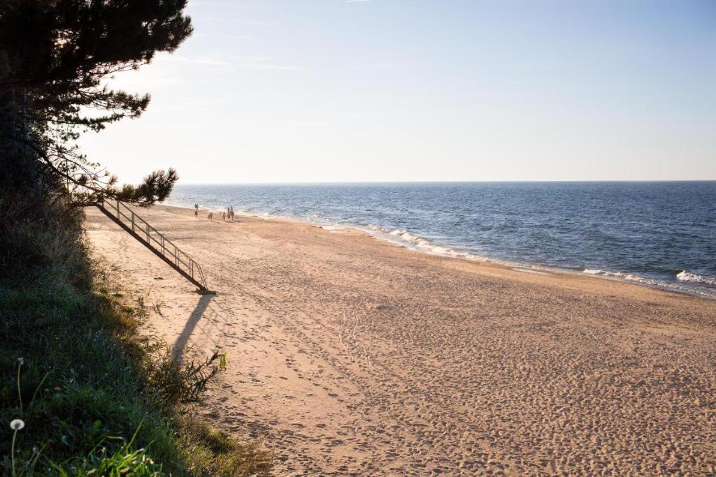 a sandy beach with people walking on it next to the ocean at Domek Przy Plaży in Gąski