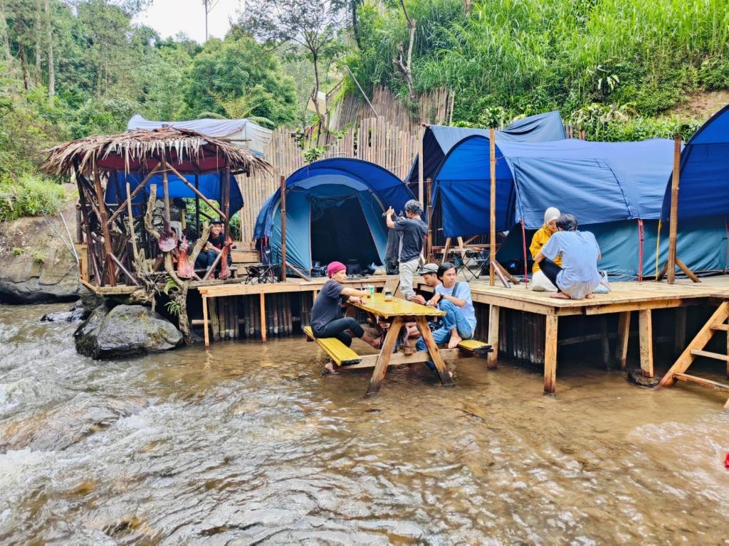 Un groupe de personnes assises à des tables dans une rivière avec des tentes dans l'établissement Camping hutan pinus singkur rahong, à Bandung