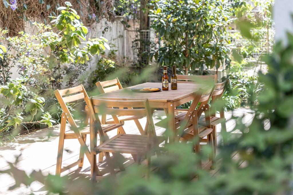 Heart of Tel Aviv Garden Oasis by Sea N' Rent في تل أبيب: طاولة خشبية مع كراسي وزجاجتين من البيرة