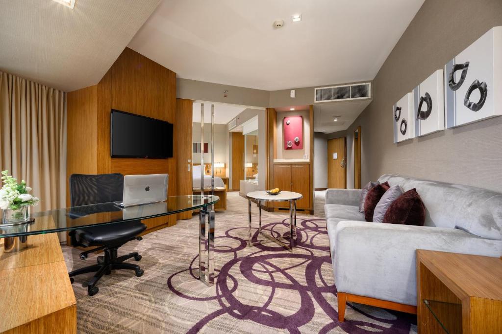 A suite living area combining a glass desk, laptop, television, and sofa seating.