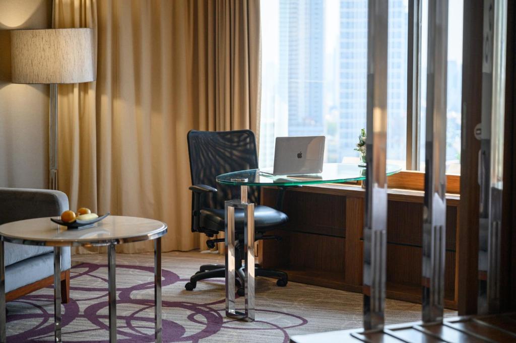 A compact desk beside tall windows, with a laptop and city backdrop.