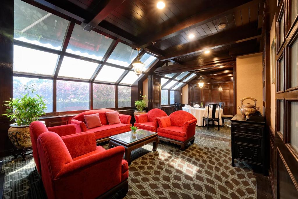A bright lounge with red armchairs beneath a glazed roof and beside large windows.