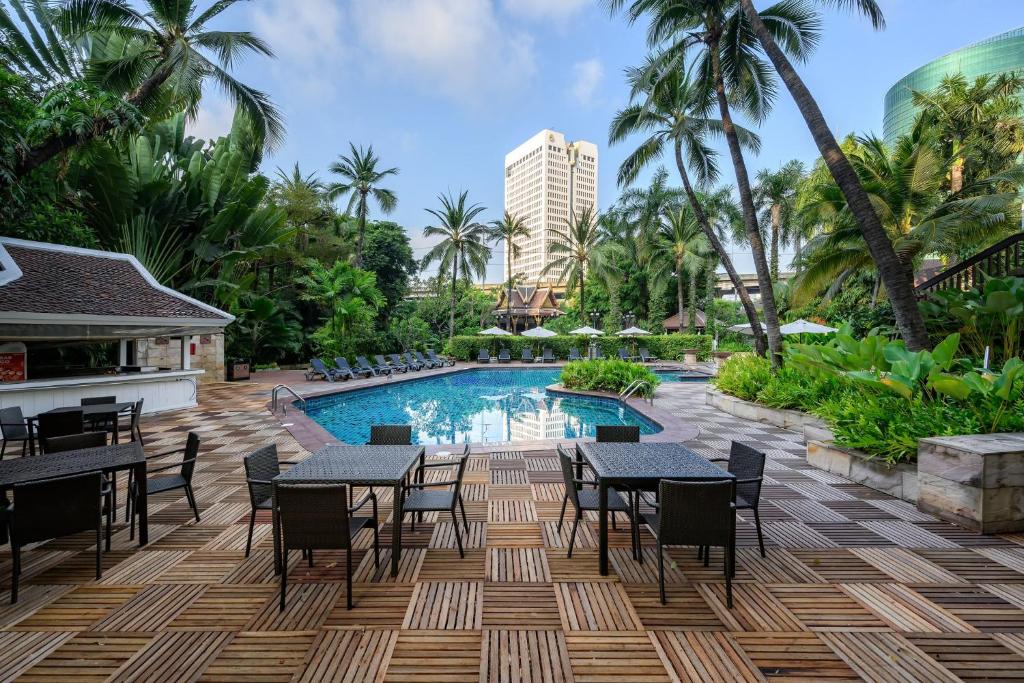 A tropical pool terrace with outdoor dining tables, loungers and palm-filled landscaping.