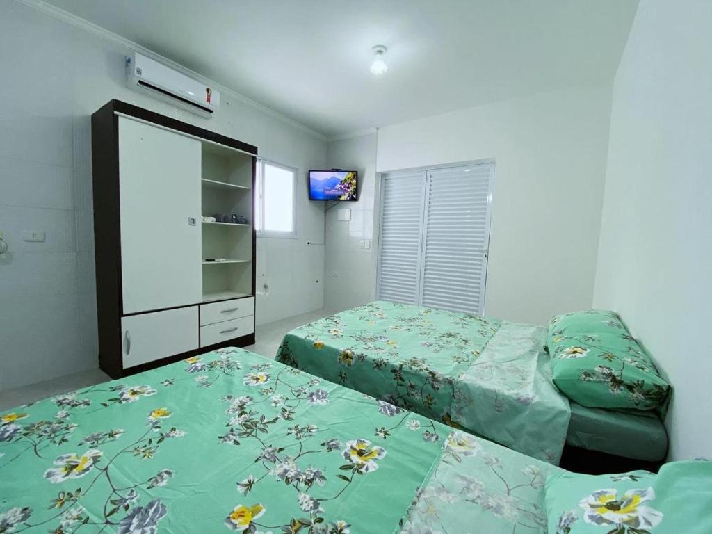 1 dormitorio con 2 camas y TV en la pared en Pousada e Espaco AURORA Peruibe en Peruíbe