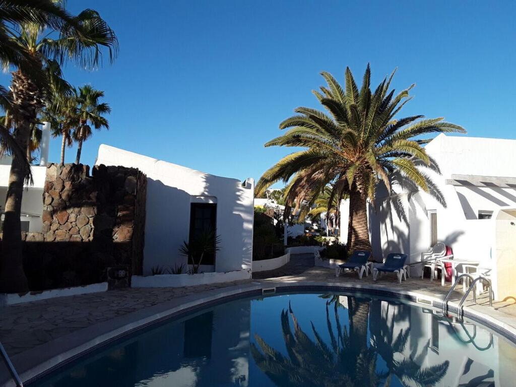 a swimming pool in front of a white building with palm trees at Holiday home with a roofed terrace in Morro del Jable