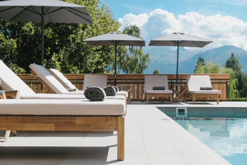 una piscina con tumbonas y sombrillas junto a una piscina en Aïda Hôtel & Spa - "Adults Only" Relais & Châteaux en Crans-Montana