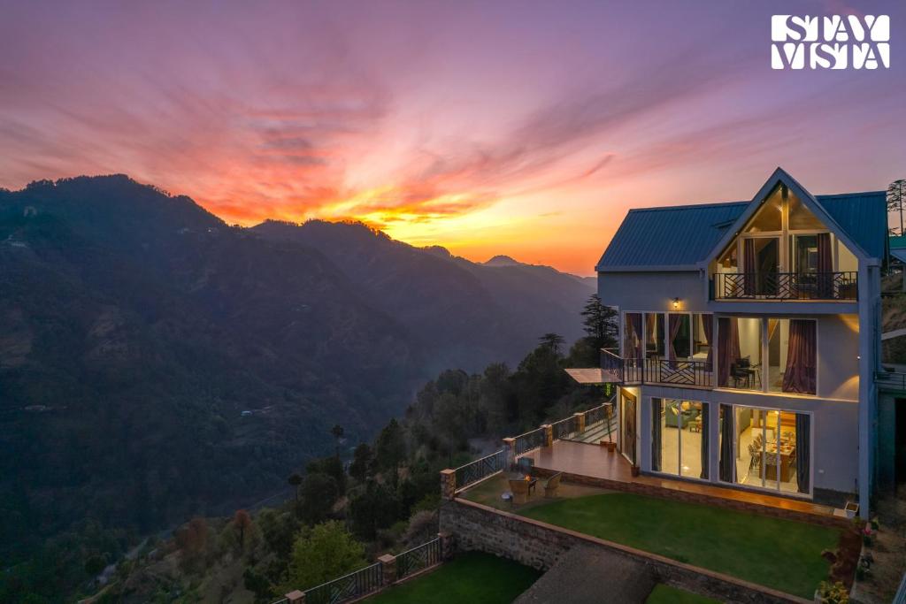 a house with a sunset in the mountains at StayVista at Orion Villa in Shimla