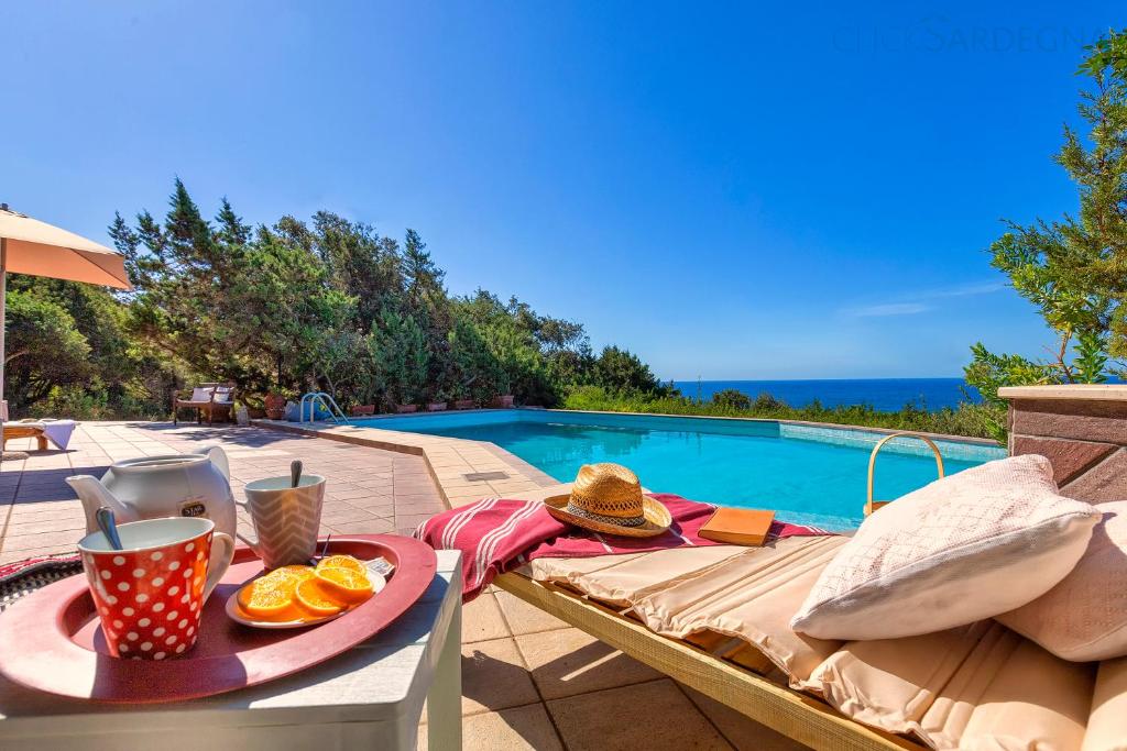 une table avec un plateau de nourriture dessus à côté d'une piscine dans l'établissement Villa Joie de Vivre Vista mare con piscina a sfioro per 6 persone, à Alghero