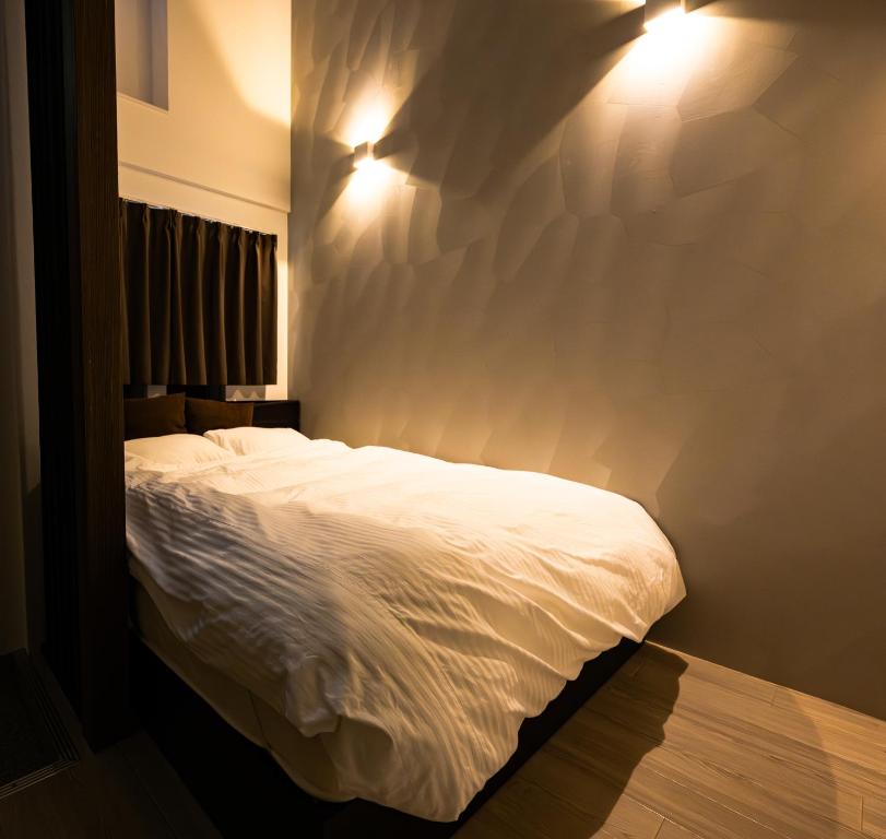Official TRhouses 15 minutes to Shinsaibashi, Kuromon Market and Namba في أوساكا: غرفة نوم مع سرير أبيض مع أضواء على الحائط
