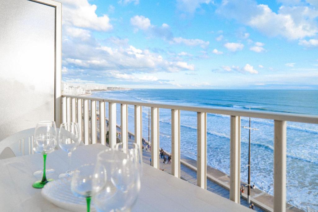 - une table avec des verres à vin sur un balcon donnant sur l'océan dans l'établissement Appartement vue baie des Sables d Olonne 5 personnes, à Les Sables-dʼOlonne