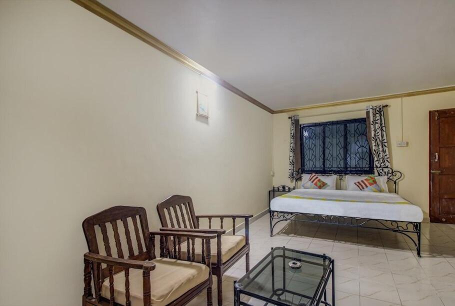 a bedroom with a bed and two chairs and a table at Super OYO Pravin Holiday Homes in Calangute