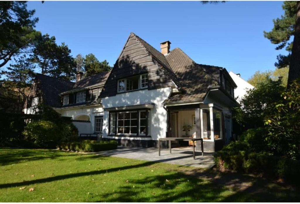 een groot wit huis met een veranda en een gazon bij Charming house Heemdael in Knokke-Le-Zoute in Knokke-Heist