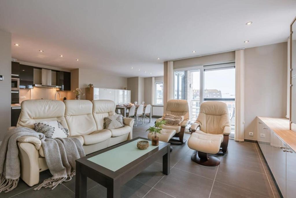 ein Wohnzimmer mit einem Sofa, Stühlen und einem Tisch in der Unterkunft Spacious apartment with lateral sea view in Blankenberge