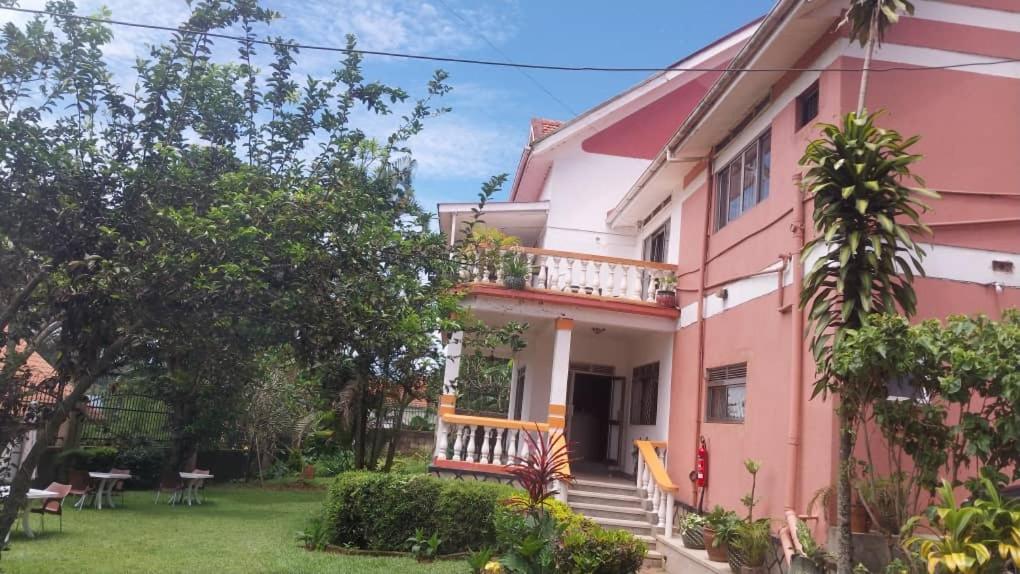 ein rosafarbenes Haus mit einem Balkon und einem Hof in der Unterkunft Lakeshore Bed and Breakfast in Entebbe