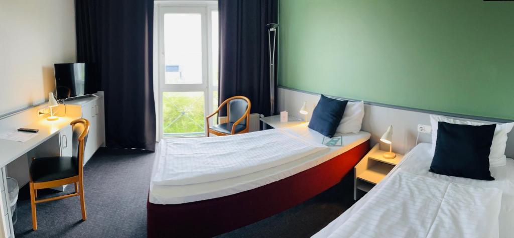 a hotel room with two beds and a desk and a window at Good Morning + Bad Oldesloe in Bad Oldesloe