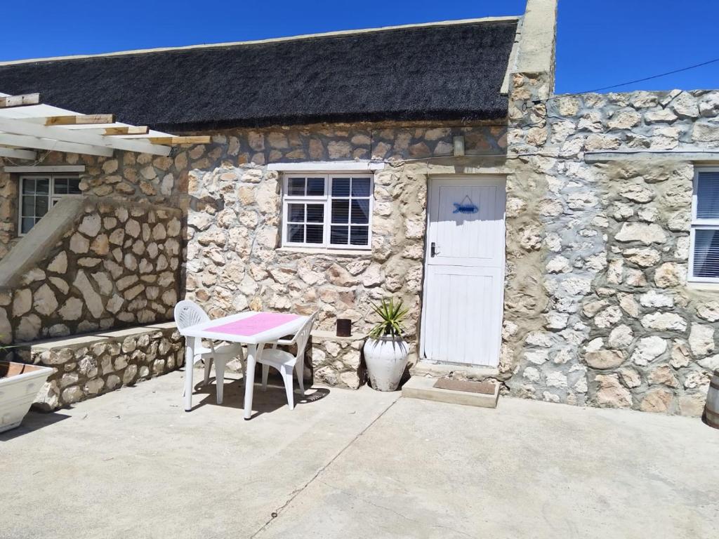 een stenen huis met een tafel en een witte deur bij Mariette's Cottage in Arniston