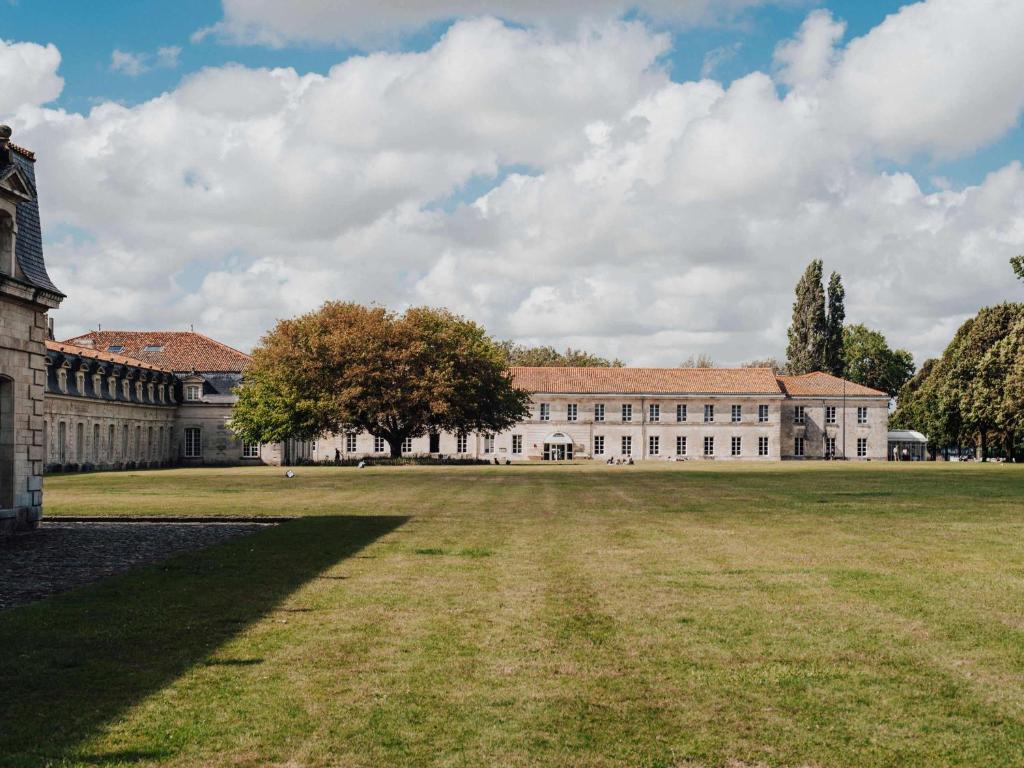 un gran edificio con un campo de césped delante de él en Hôtel Mercure Rochefort La Corderie Royale, en Rochefort