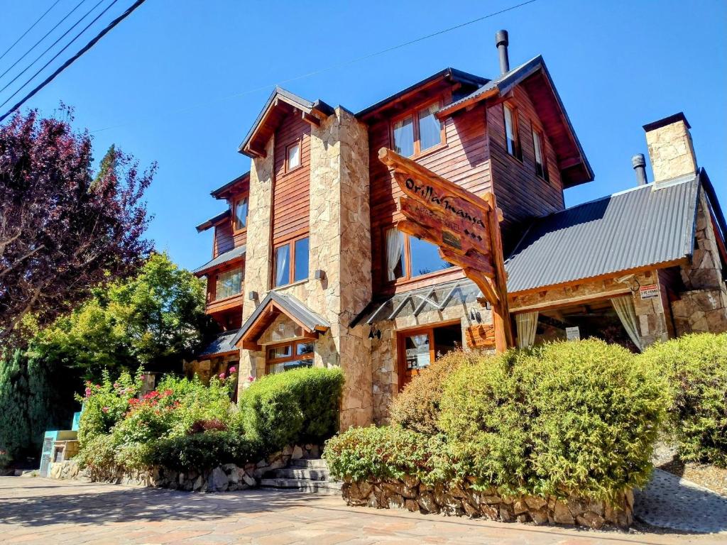 una grande casa in legno con cespugli di fronte di Apart Hotel Orilla Mansa by Visionnaire a San Martín de los Andes