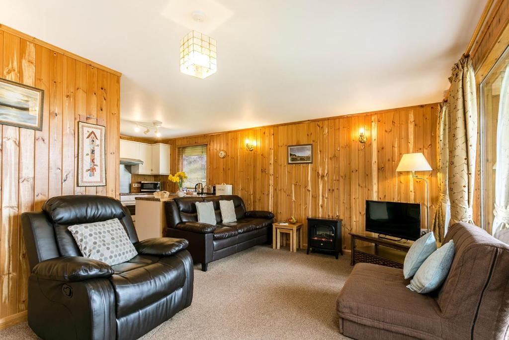 a living room with leather furniture and a television at Yew Tree Lodge in Minehead
