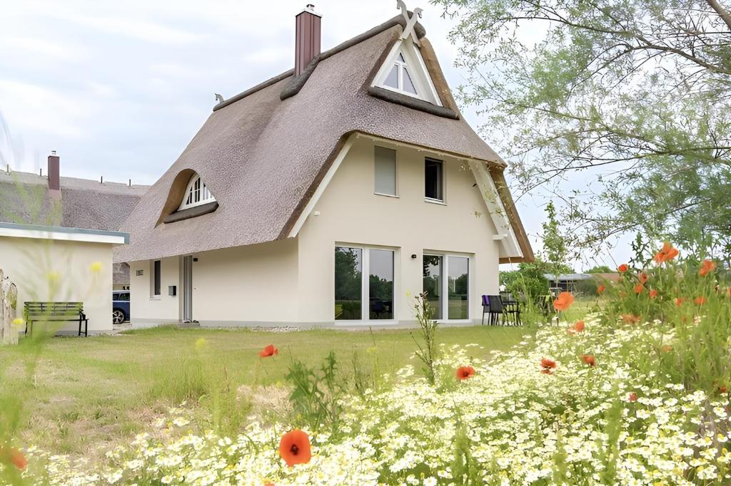 uma casa com telhado de palha e um campo de flores em De Henkieker - Ferienhaus mit Sauna und Kamin für 6 Personen em Pepelow