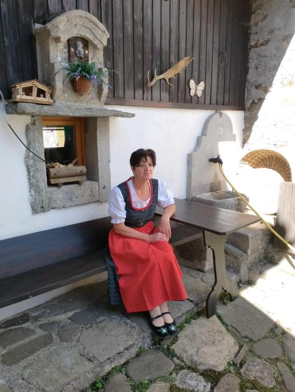a woman sitting on a bench with an outdoor oven at Casa Laura in Ravascletto