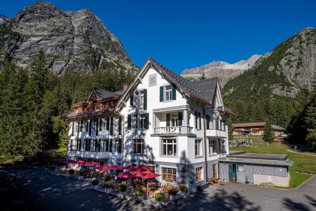 un grand bâtiment blanc avec des parasols rouges en face des montagnes dans l'établissement Hotel und Naturresort Handeck, à Guttannen