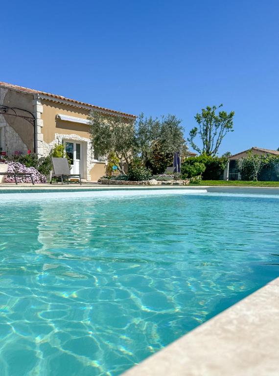 une piscine avec de l'eau bleue devant une maison dans l'établissement Le Petit Valexiane Piscine & Jardin, à Maillane