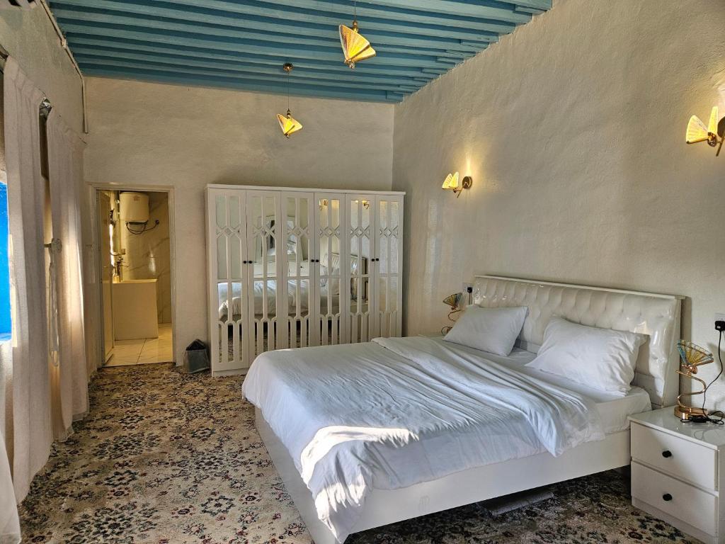 a bedroom with a white bed and a blue ceiling at منزل حجري بحديقتين in Ḩajlah