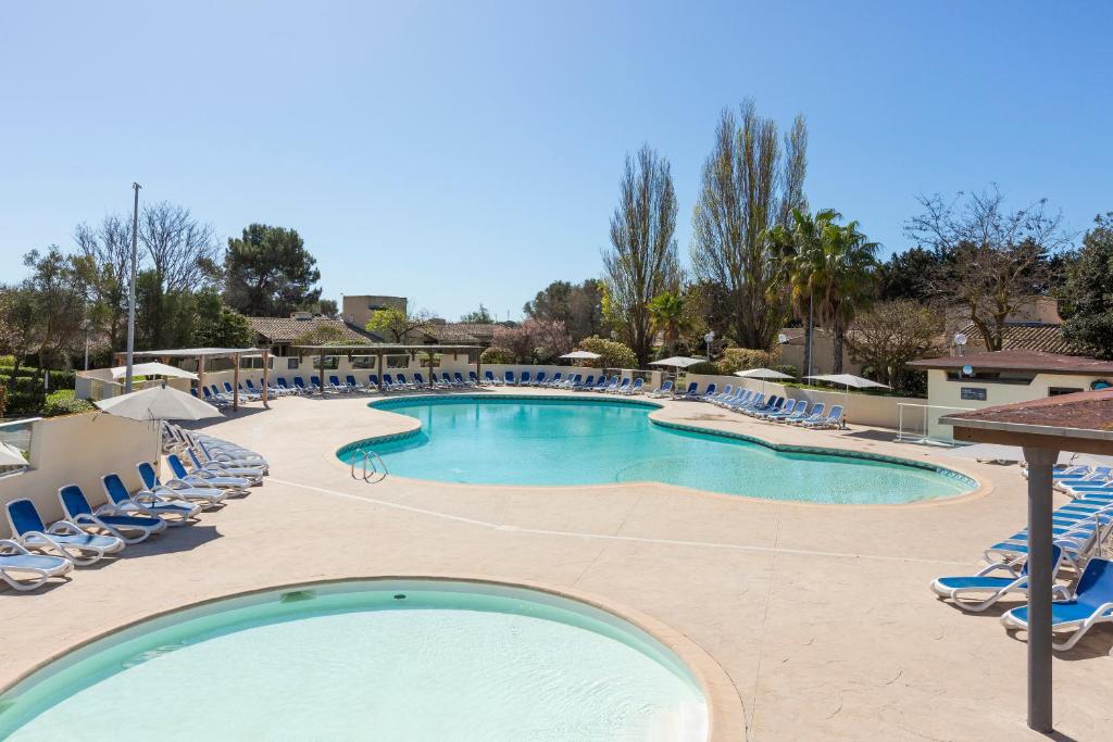 a large swimming pool with lounge chairs and a resort at SOWELL HÔTELS Les Jardins du Cap in Cap d'Agde