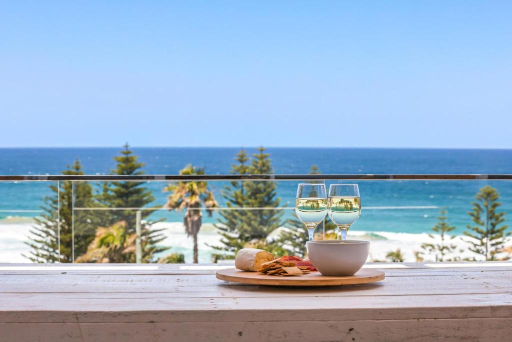 a table with a plate of food and two glasses of wine at Sweeping Panoramic Views - Brand New Beach House in Curl Curl