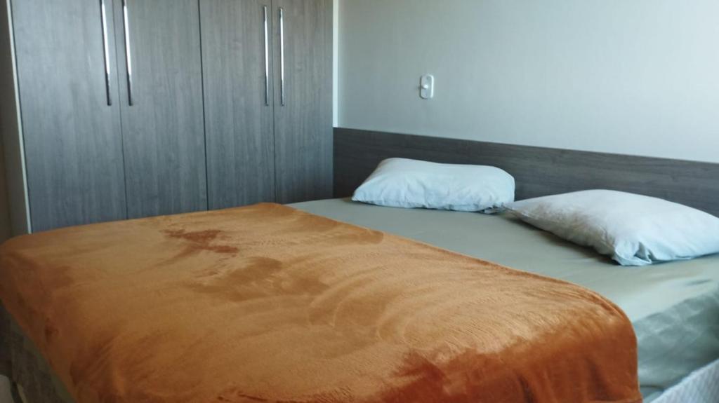 a bed with an orange blanket and two pillows at Quarto Confortável Centro e perto de Hospital in Dourados