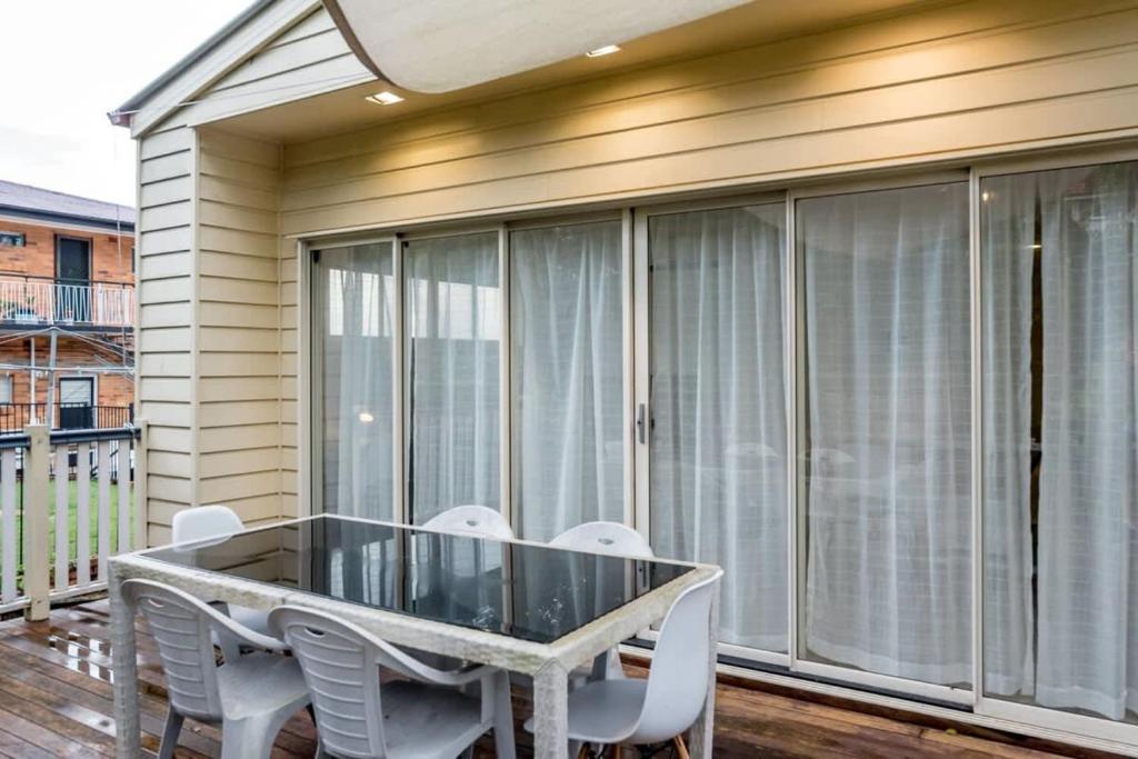y balcón con mesa de cristal y sillas blancas. en Modern 2BR With Deck en Brisbane