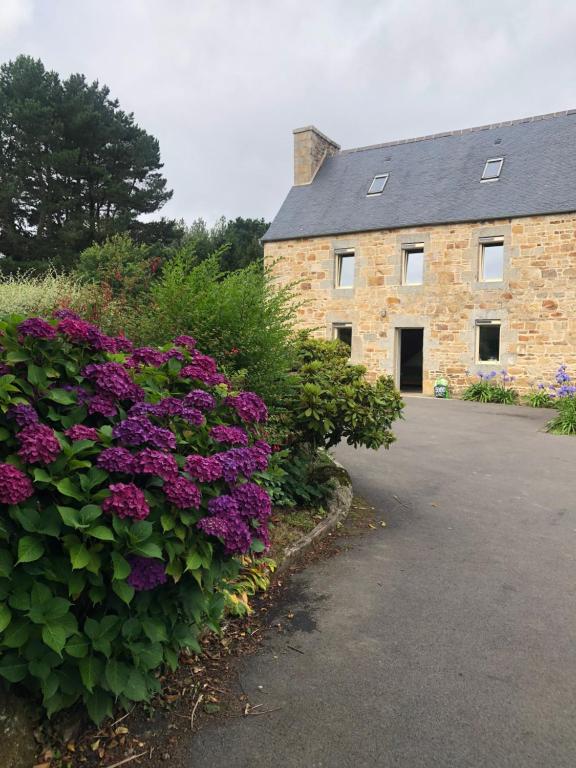 un edificio de piedra con flores púrpuras delante de él en Les Trégorines-Squibernévez, en Pédernec