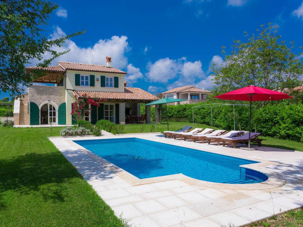a pool with chairs and an umbrella in front of a house at Villa Bella by Interhome in Marčana