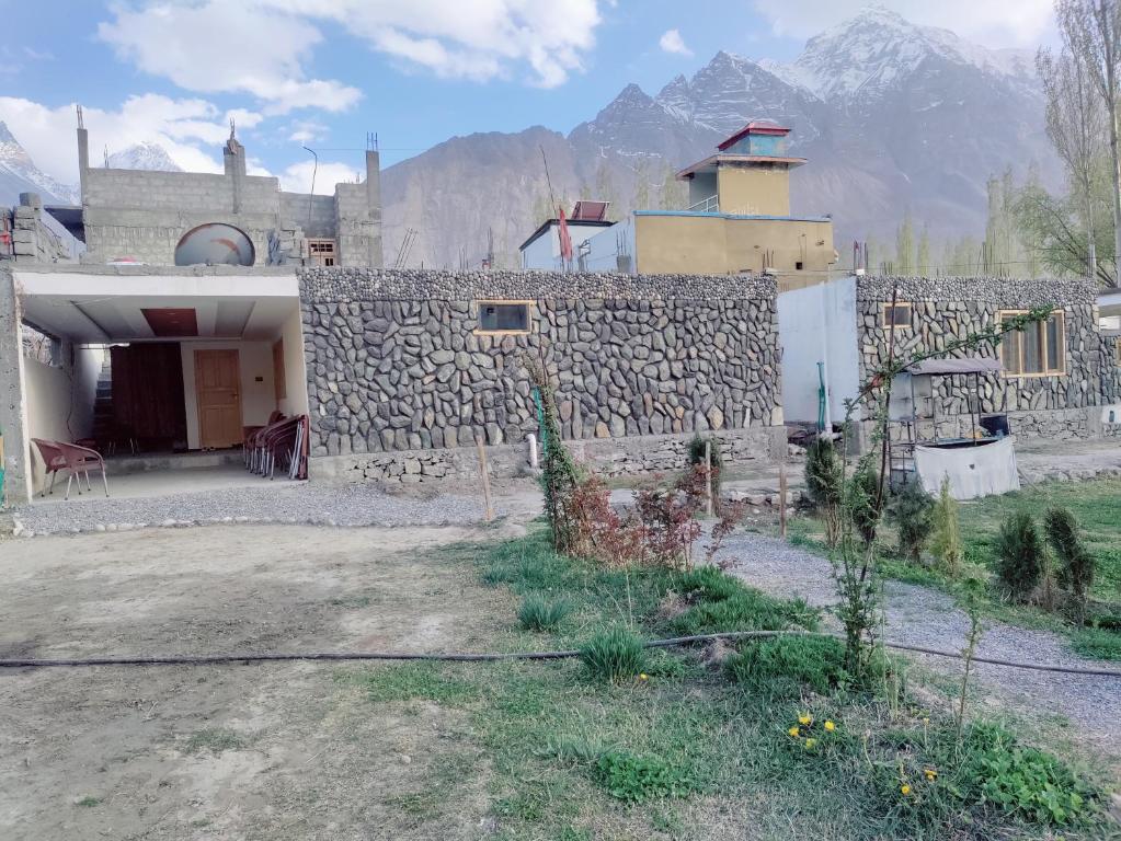 a house with a stone wall with mountains in the background at Baltistan Sarayee hotel £ Guest House in Skardu